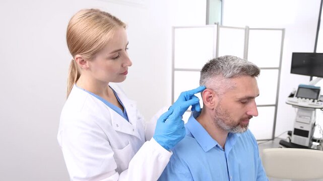 Audiologist putting hearing aid on man's patient ear at audiology center, close-up, side view. Deafness treatment, hearing solutions