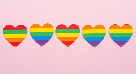 Five rainbow colored hearts aligned in a row on a pastel pink background symbolizing love, diversity, and lgbtq pride