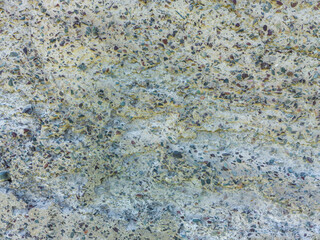 A close-up shows a concrete texture with a high concentration of colorful pebbles and stones exposed on its rough surface. This is a prominent example of exposed aggregate concrete.