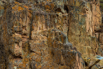 Rugged rock formation displays intricate layers and color variations in a natural outdoor setting. The austere landscape evokes a sense of earthy beauty during daytime.