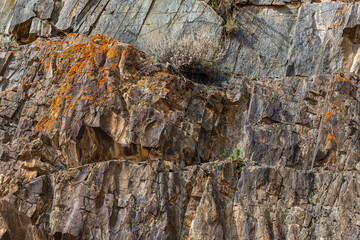 Rugged rock formation covered in orange lichen stands tall in a mountainous Kyrgyzstan region.
