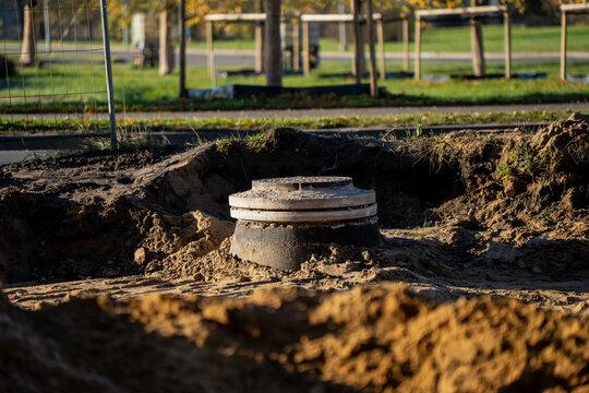 Newly installed concrete sewer manhole at construction site surrounded by excavated soil, part of underground water and drainage infrastructure installation in urban area