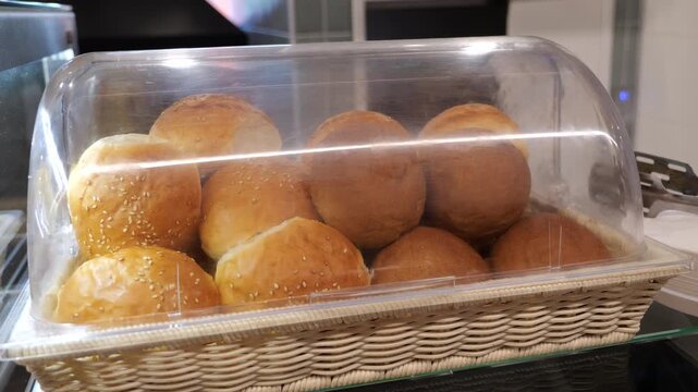 Close-up of a cook in a bakery putting freshly baked buns in a bread box on a shelf in the bakery. The concept of catering and buffet.