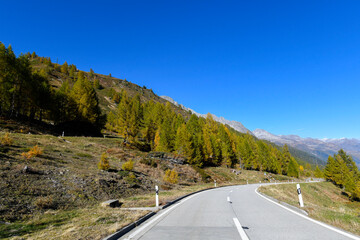 High mountain panorama in late summer, early autumn, with green and yellow larches, blue sky, in the Swiss Alps.