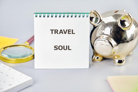 A notebook titled Travel Soul sits beside a golden piggy bank and a magnifying glass on a soft, light surface, inviting dreams of exploration and adventures to new destinations in the world