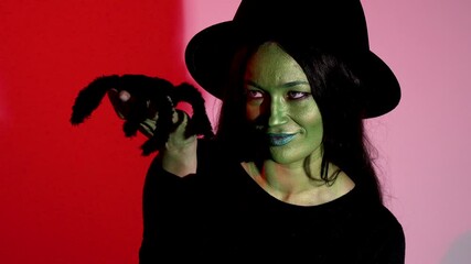 a woman dressed as a witch holds a large black spider in her hands.