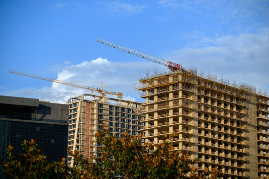 Active construction zone with cranes and scaffolding, high-rise construction under clear blue sky with cranes and steel structures. Urban development and construction concept - Powered by Adobe