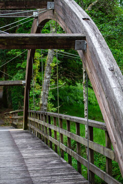 Architectural detail of a rustic wooden arch footbridge in a lush green forest.