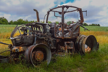 Close-up photo of a burnt-out agricultural vehicle (tractor) at the edge of an agricultural field.