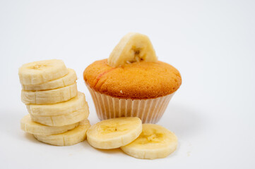Cupcake topped with a slice of banana, accompanied by stacked and scattered banana slices, isolated on a white background.