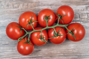 Fresh cluster of ripe cherry tomatoes on a vine, placed on a wooden surface.