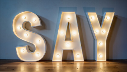 Lit marquee letters spelling 'SAY' on wooden floor with blue wall  
