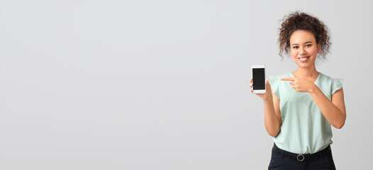 Young African-American businesswoman with mobile phone on grey background