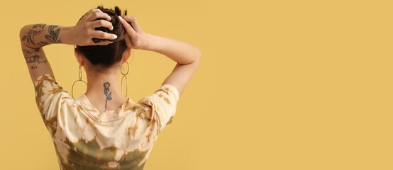 Tattooed young woman on yellow background with space for text, back view