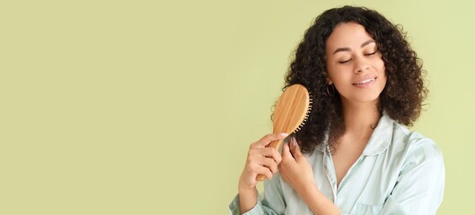 Beautiful African-American woman brushing hair on green background with space for text