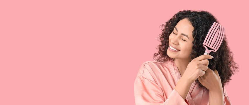 Beautiful African-American woman brushing hair on pink background with space for text