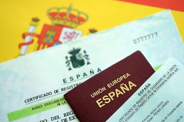 Spanish passport lies on citizenship or naturalization documents on flag of Spain close up