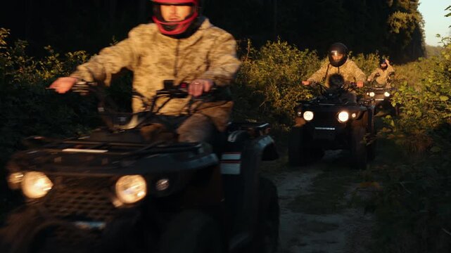 Team on terrain vehicles, Forest excursion, Sunlit ride. Group, wearing camouflage and helmets, drives ATVs through brightly lit trail amidst dense vegetation.