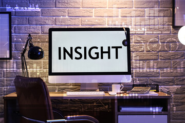 Blank computer monitor with glowing lamp on desk in office at night