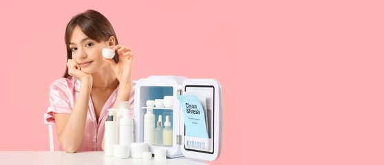 Beautiful young woman with small refrigerator for cosmetics on pink background with space for text