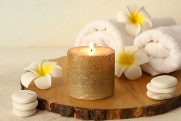 Spa composition with golden candle, wooden tray, spa stones and flowers on light background, closeup