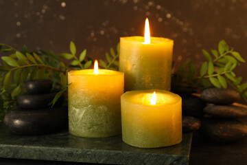 Spa composition with candles, spa stones and green leaves on dark background, closeup