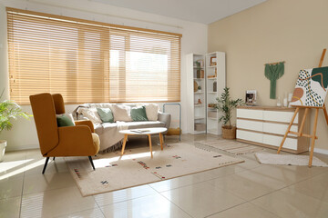 Comfortable armchair, sofa and table near window in interior of living room