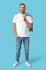 Fototapeta premium Stylish man in jeans holding denim jacket on blue background