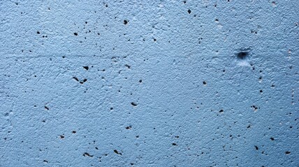 close up rugged uneven wall with lots of holes painted in vibrant blue for wallpaper