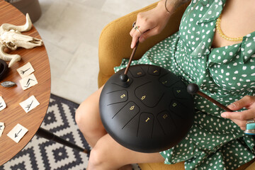 Young witch playing glucophone in armchair at home, closeup