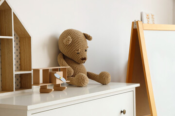 Chest of drawers with teddy bear and wooden airplane in kindergarten, closeup