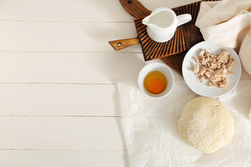 Baking paper with fresh dough, yeast, raw egg and jug of milk on white wooden background