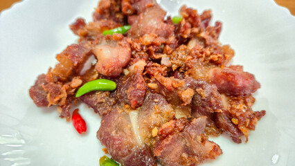 crispy fried pork with chili peppers on white plate close up