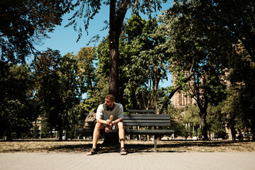 Young man sitting on a bench in the park eating ice cream on a sunny summer day. Concept of leisure, happiness, and lifestyle