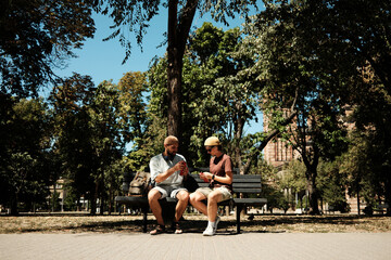 Young man and woman sitting together on a bench in the park eating ice cream and talking. Concept of friendship, leisure, and summer lifestyle