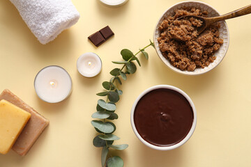 Spa composition with bowl of chocolate sea salt and burning candles on pale yellow background