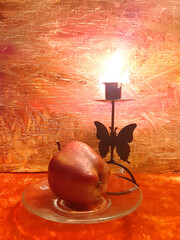 Red apple on a saucer, fruit, food. Evening romantic still life on a red background, candle in a candlestick. Romance, flowers, elegance, flair. Antique brass item