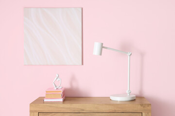 Desk lamp, books and statuette on chest of drawers near pink wall in room