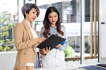  Teamwork process. Two Asian businesswoman working pointing laptop computer and discussing...
