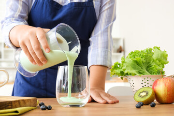 Young woman pouring healthy smoothie into glass in kitchen