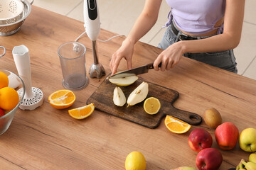 Young woman cutting fresh pear for smoothie in kitchen