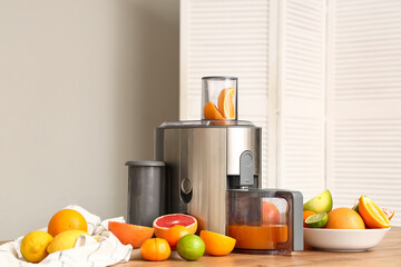 Modern juicer and different tasty citrus fruits on table in kitchen, closeup