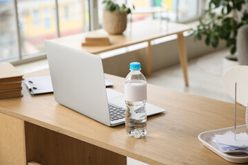 Bottle of water and modern laptop on table in room