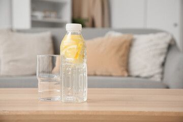 Bottle of water with pieces of lemon on table in room, closeup