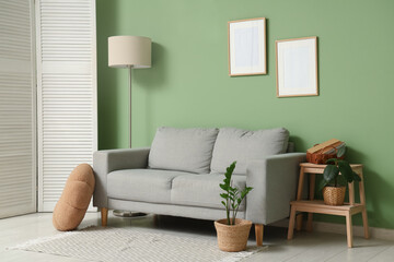 Interior of living room with floor lamp, folding screen and sofa near green wall
