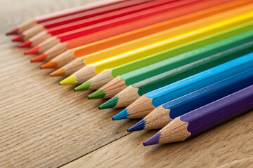 Obraz premium A vibrant array of colored pencils arranged diagonally on a light wood surface, showcasing the full spectrum of the rainbow in a visually pleasing and artistic composition.