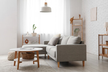 Comfortable sofa and table near window with white curtains in interior of living room