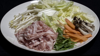 白い大皿に盛り付けられた豚肉や白菜などの新鮮な鍋物用の具材