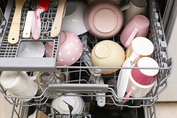 Open dishwasher filled with clean cups and kitchen utensils. Domestic appliance concept. Modern...
