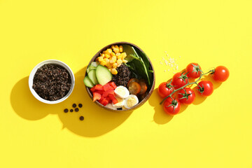 Bowls with healthy quinoa salad and ingredients on yellow background